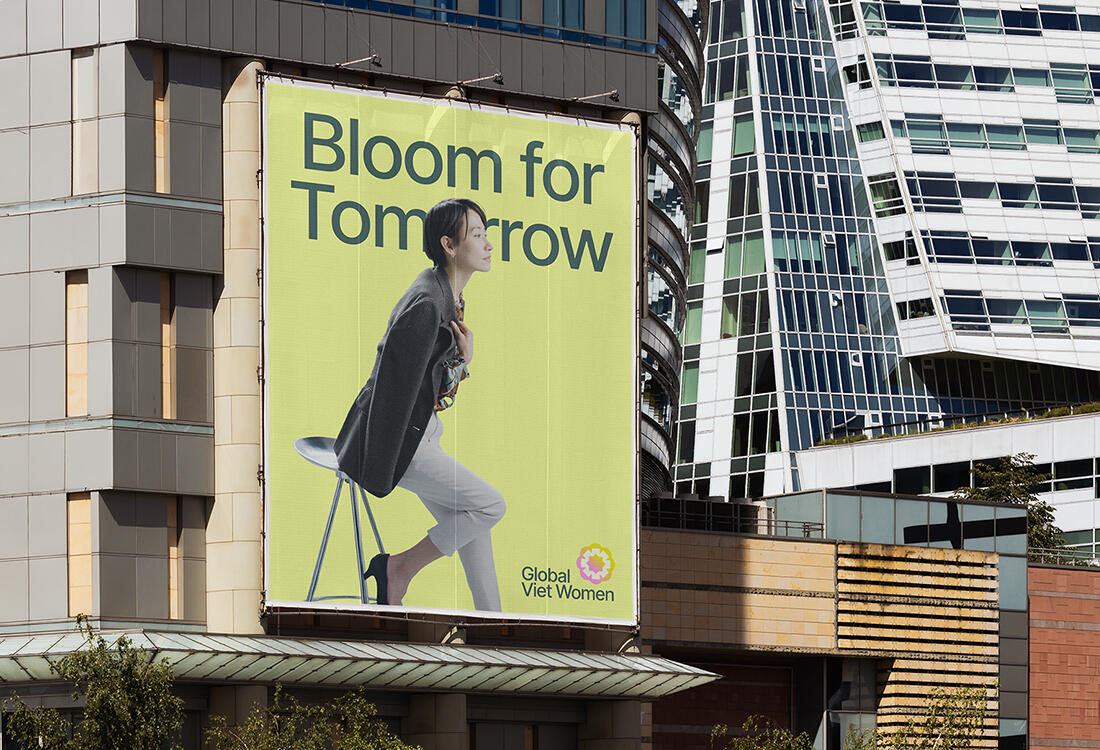 Cover image for the project "Global Viet Women". The image consists of a large billboard in a city. The billboard is a simple poster advertising for the organization. It features a confident Vietnamese women leaning on her chair. She is wearing professiona
